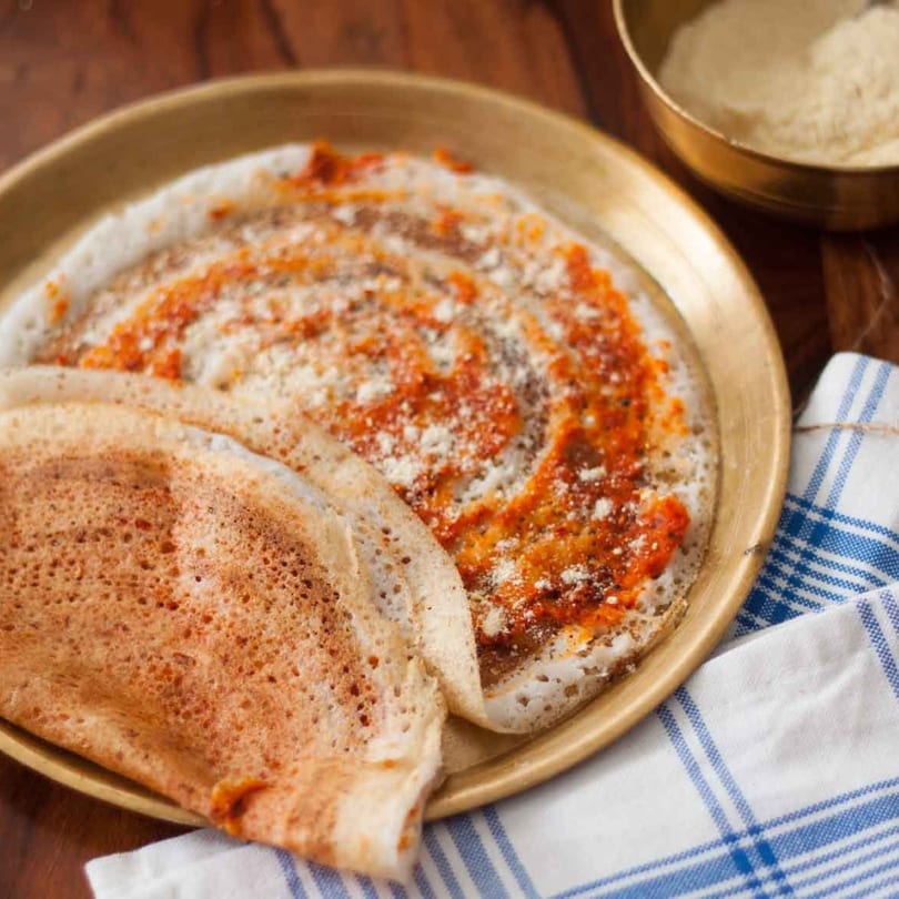 Two Indian dosas, one plain and one with red chutney and white powder, on a brass plate.