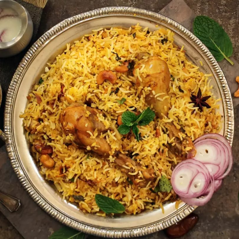Bawarchi Biryanis' chicken biryani with rice, cashews, mint, and sliced red onions on a silver platter.