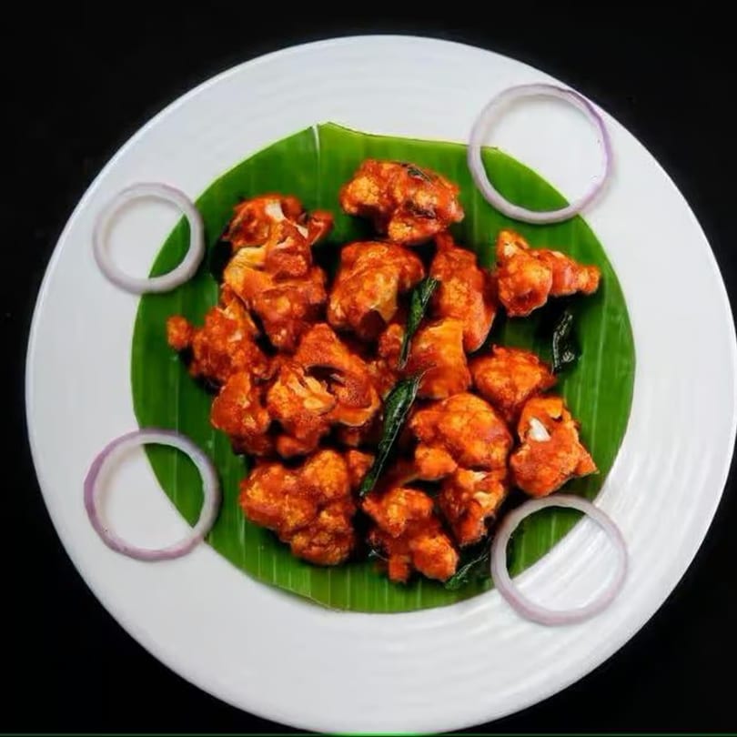 Bawarchi Biryanis' Gobi 65, a spicy Indian fried cauliflower dish, garnished with curry leaves and onion rings.