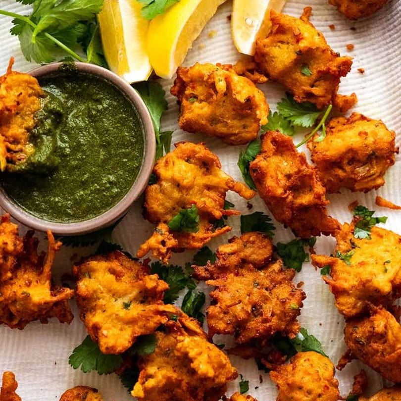 Crispy golden Indian pakoras with fresh cilantro, lemon wedges, and a bowl of green chutney.