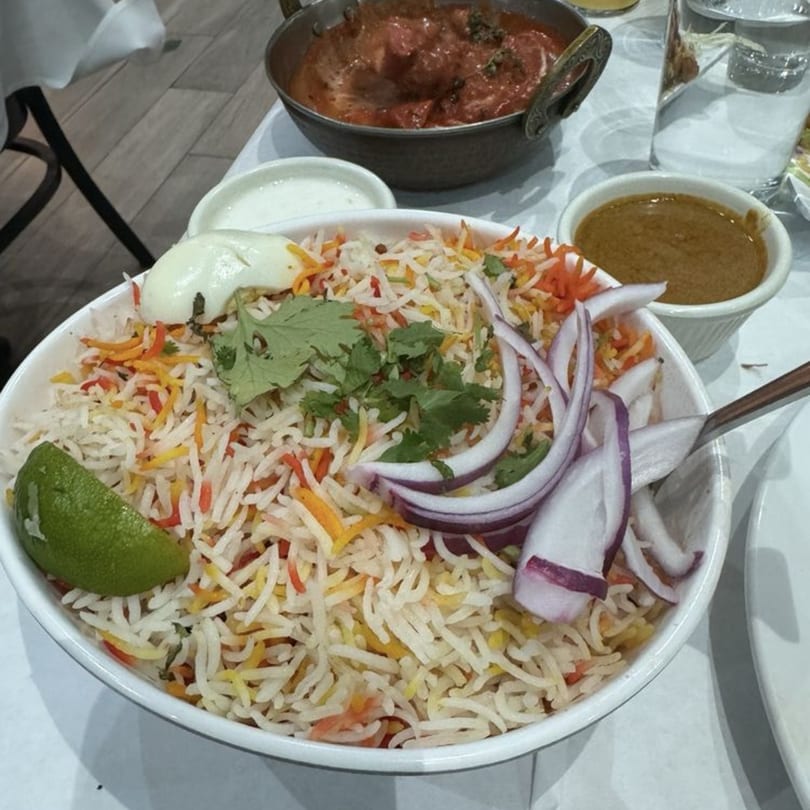 Bawarchi Biryanis' chicken biryani with lime, red onions, cilantro, and sides of curry and raita.