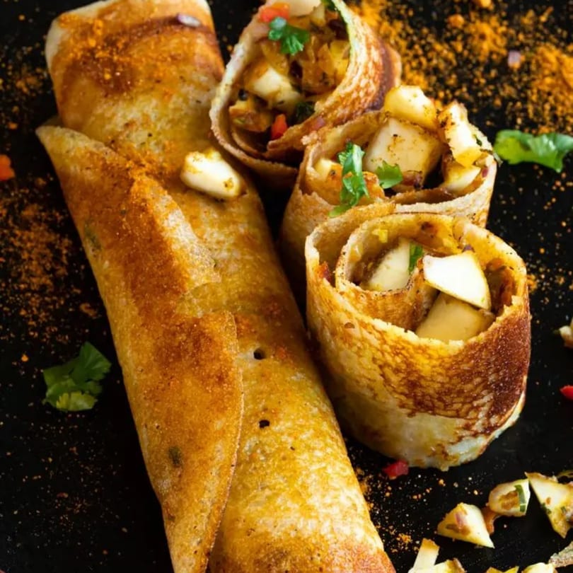 Crispy Indian dosas, one whole and three cut, filled with paneer and vegetables, on a dark surface.