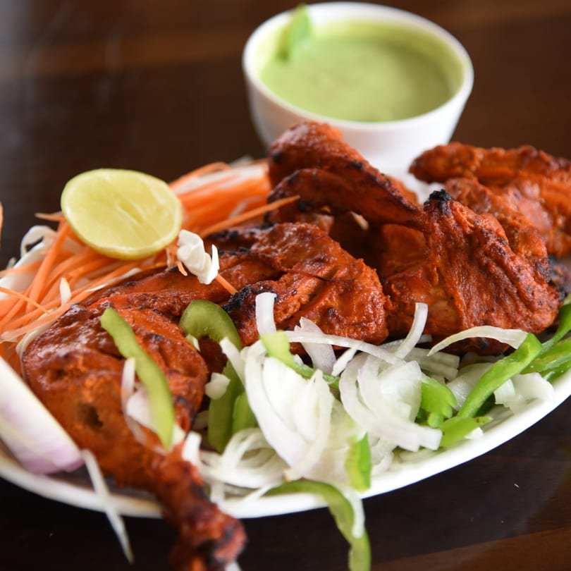 Bawarchi Biryanis' Tandoori Chicken, garnished with lime, onions, and carrots, with a side of green chutney.