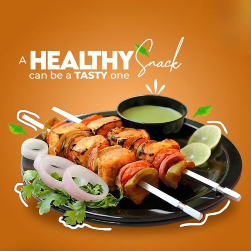 Indian chicken tikka skewers with green chutney, lime, and onions on a black plate.