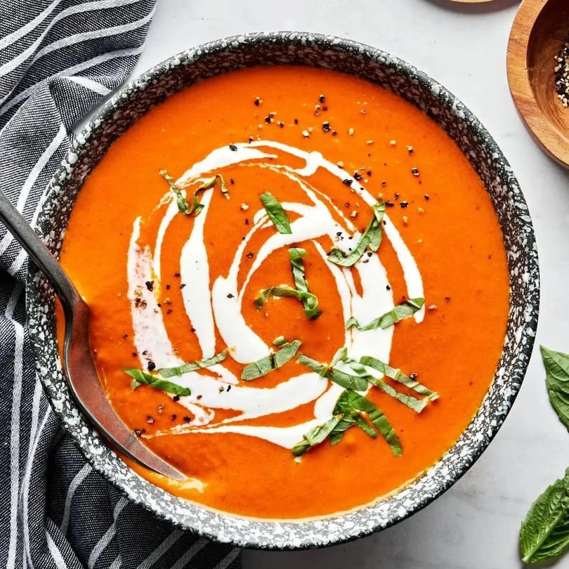 Close-up of a bowl of creamy tomato soup, garnished with fresh basil and a swirl of cream.