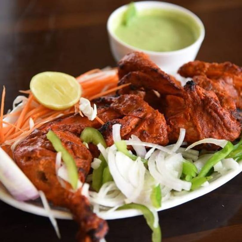 Tandoori chicken with lemon, shredded carrots, onions, and green peppers, with a side of green chutney.