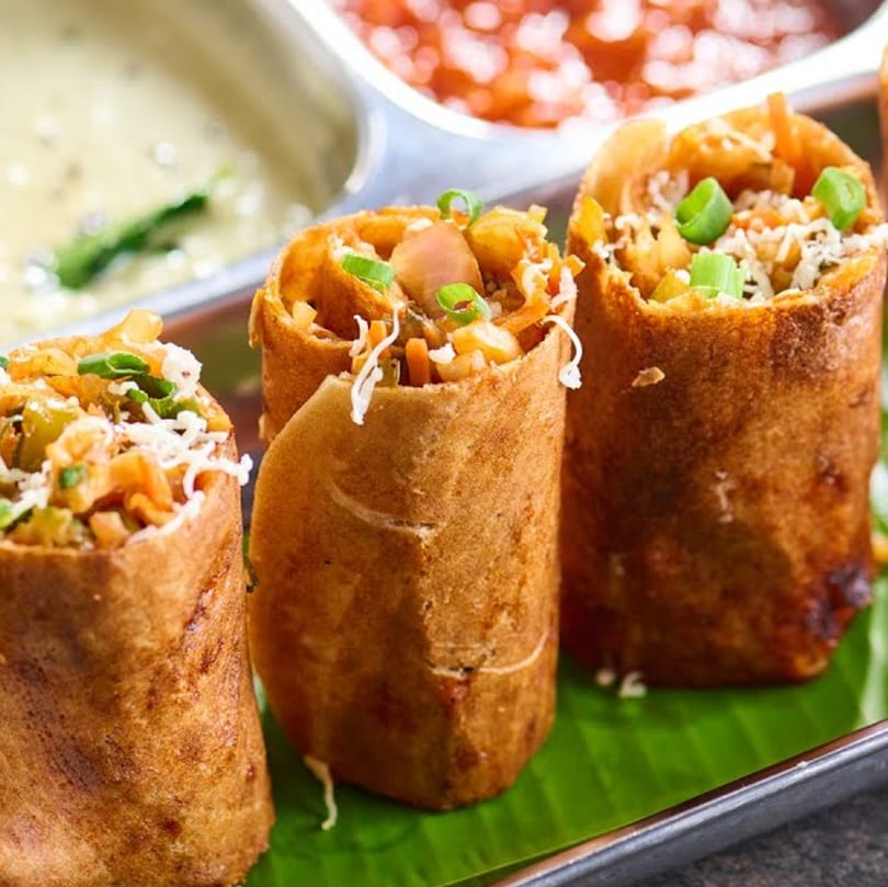 Three crispy Indian dosas, filled with vegetables and cheese, served with chutneys on a banana leaf.